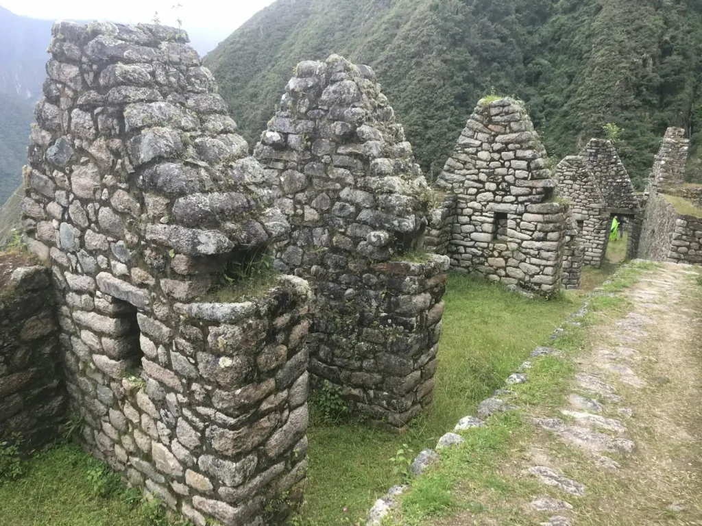 Stone Inca buildings on a green hillside along the Inca Trail
