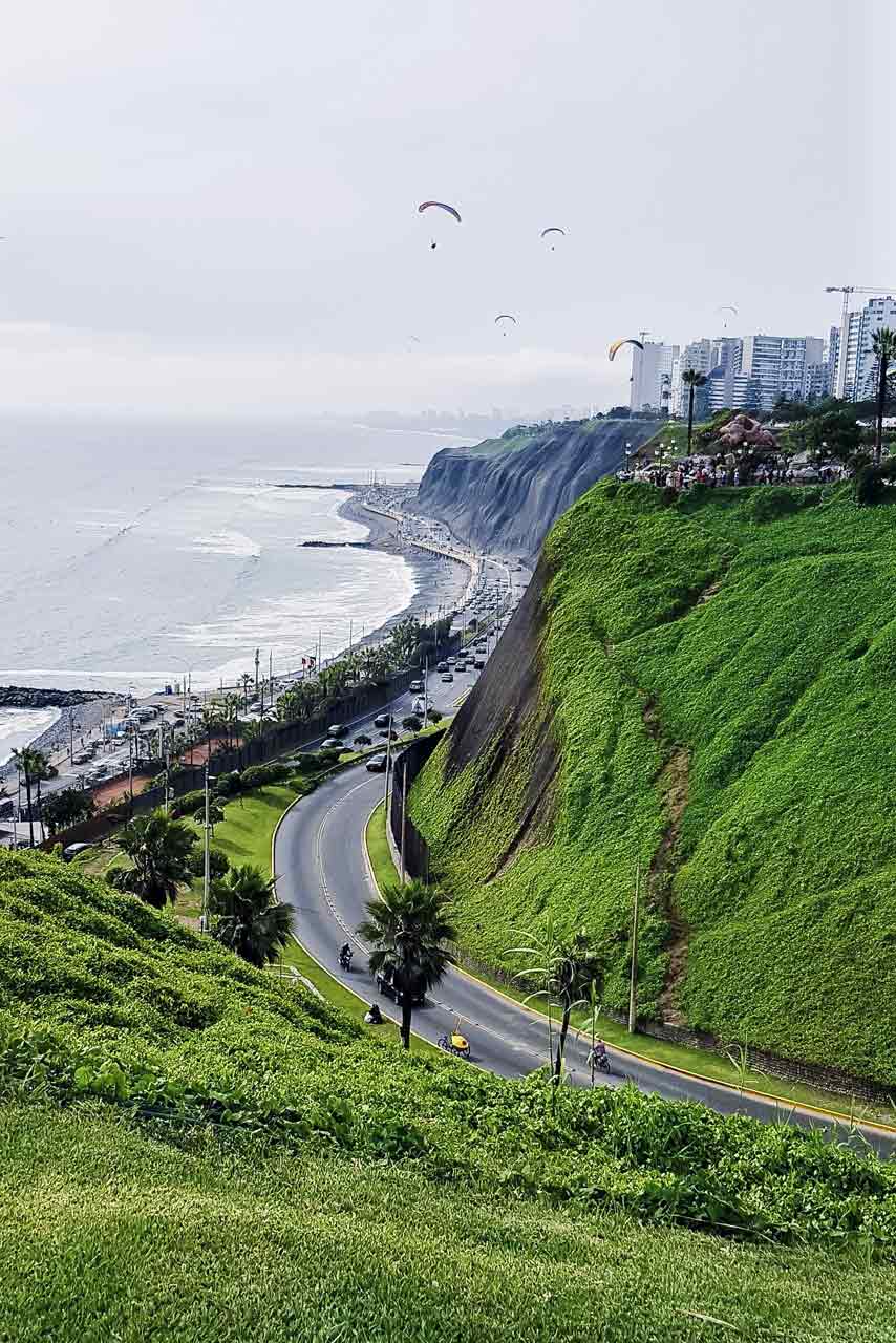 Green cliffs of Miraflores above the Costa Verde road and the Pacific, with paragliders over Lima
